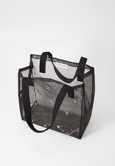 Transparent sort mesh tote taske med broderede blomster mønstre, sorte stofhåndtag og et logo tag indeni. Rummelig og letvægtsdesign.