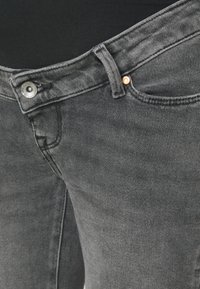 Jeans din denim gri, cu o vedere detaliată a taliei, care prezintă un buton metalic și detalii cu nituri din cupru, precum și o țesătură texturată.