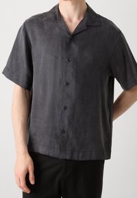 Camisa de manga corta, de color gris carbón, fabricada en una tela suave. Presenta un cuello estándar, siete botones y un diseño de ajuste relajado.