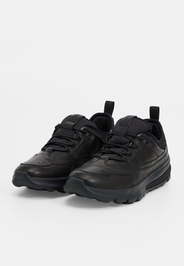 Ein Paar schwarze Leder- und Stoff-Sneaker mit Schnürsenkeln, Zugschlaufen an den Fersen und dicken strukturierten Sohlen, vor einem schlichten weißen Hintergrund abgebildet.