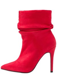 Botín de ante rojo hasta el tobillo con un puño holgado, punta afilada y tacón alto de aguja. Textura suave y diseño sin costuras.