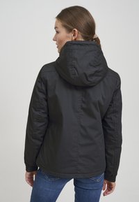 Svart polstret jakke med hette, elastiske mansjetter og rett snitt. Glatt tekstur, enkel design og ensfarget. Bakperspektiv vist.