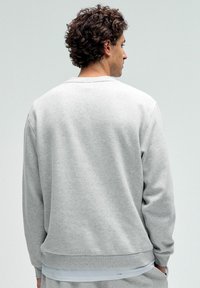 Hallide hall sweatshirt, mis on valmistatud pehmest kangast, omab ümarat kaelust, soonikuid varrukaotstes ja allääres. Kujundus on lihtne ja sile tekstuur.