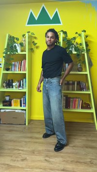 Chemise noire à manches courtes associée à un jean ample en denim délavé et des chaussures noires. Fond jaune vif avec un graphique de montagne verte et des étagères.