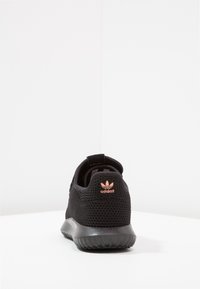 Svart sportskor med övre del av mesh och texturerad baksida. Har en vadderad krage och en rosa Adidas-logga på hälen. Gummisula.