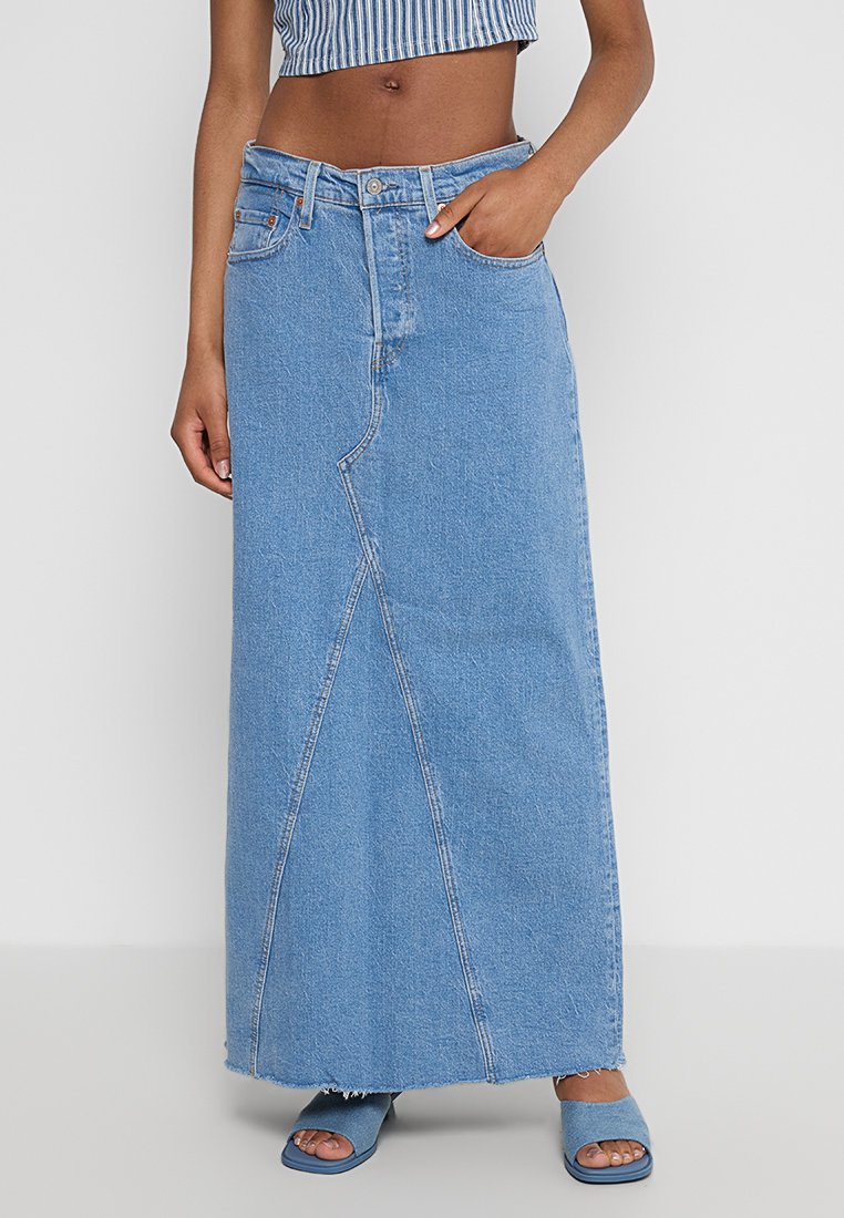 Falda maxi de mezclilla azul clara con una cintura alta, bolsillo frontal y diseño de costura asimétrica. Borde sin acabar en el dobladillo.