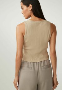 Top sin mangas de canalé beige con escote redondo y bajo recortado, combinado con pantalones gris claro que tienen bolsillos traseros.