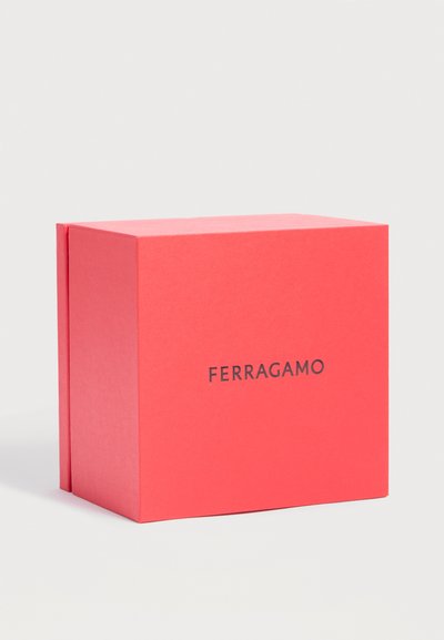 Boîte rectangulaire rouge de marque Ferragamo avec un logo noir en gras sur le devant, sur un fond gris clair uni.