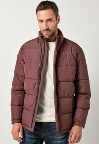 Mørkerød pufferjakke med lynlås foran, trykknaplukning, høj krave og quiltet tekstur. Sammen med en lys skjorte og jeans.