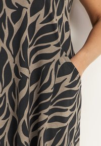 Kukkakuosisessa mekossa on mustia lehtikuvioita vaaleanbeige taustan päällä. Mekko on valmistettu pehmeästä kankaasta ja siinä on sivutasku.