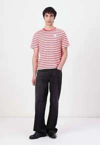 Tricou roșu cu dungi albe, din bumbac, asortat cu blugi negri cu picior larg și pantofi negri. Design minimalist, cu mâneci scurte.