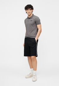 Grå polo med korte ærmer og et lille logo, kombineret med sorte shorts med sidelommer og lyse sneakers.