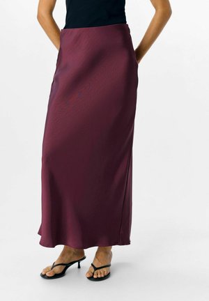 Gonna maxi in satin bordeaux con una texture morbida, una leggera lucentezza e spacco laterale, abbinata a sandali neri con cinturini.