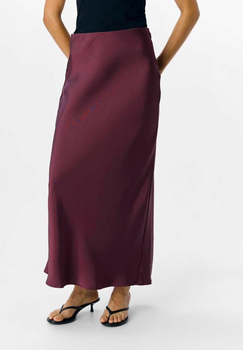 Gonna maxi in satin bordeaux con una texture morbida, una leggera lucentezza e spacco laterale, abbinata a sandali neri con cinturini.