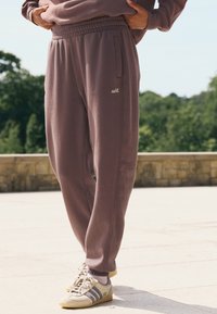 Lillat värvi vabaajapüksid kummilõngaga vöökohal, küljetaskute ja väikese valge logoga. Sobitatud heledate tossude ja triibuliste detailidega.