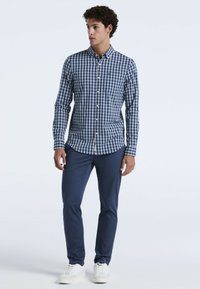 Knopen-overhemd in een marineblauw en wit geblokt patroon, van katoenmateriaal, met lange mouwen, gecombineerd met marineblauwe broek en witte sneakers.