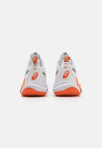 Witte sportschoenen met oranje accenten, met een gestructureerde achterzijde, ronde zool en verstevigde hielplaat, ontworpen voor ondersteuning en comfort.