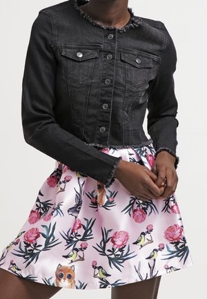 Veste en denim noir aux bords effilochés associée à une jupe rose ornée de motifs floraux, d'oiseaux et de hiboux.