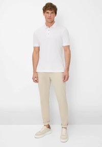 Polo bianco a maniche corte, con una patta con tre bottoni. Abbinato a pantaloni tapered beige e sneakers beige. Design semplice.
