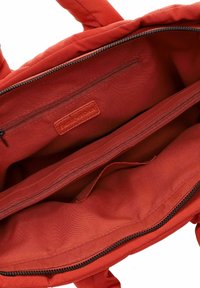 Borsa tote in tessuto rosso con due scomparti con zip e un'etichetta di marca in pelle. Texture morbida, manici robusti e un interno spazioso.