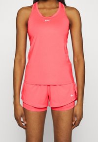 Lyserød atletisk tanktop og shorts lavet af let, fugttransporterende stof med et lille hvidt Nike-logo foran i midten.
