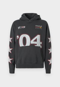 Čierna mikina s kapucňou, ktorá má vrecko vpredu, sťahovaciu šnúrku na kapucni, veľký strieborný dizajn čísla '04' a biele hviezdy na rukávoch. Logá sú zobrazené na hrudi.