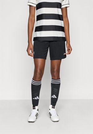 Shorts de football noirs et maillot rayé noir et blanc avec un col rond, assortis à des chaussettes noires à rayures blanches et logo, ainsi que des crampons blancs.