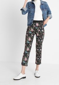 Blommönstrade byxor med svart bakgrund, prydda med rosa och blå blommor, i kombination med en jeansjacka och vita skor.