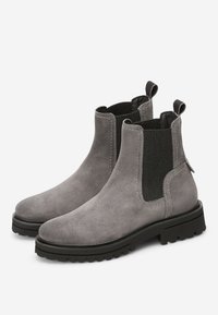 Šedé semišové Chelsea boty se elastickými bočními panely, poutky na patach a robustní černou gumovou podrážkou. Švy zvýrazňují design.
