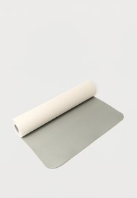 Tapis de yoga bicolore partiellement déroulé avec une face beige clair et une autre gris pâle, sur un fond blanc uni.