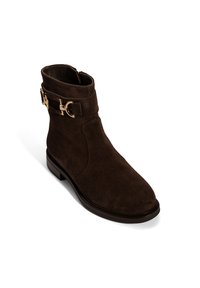 Braune Wildleder-Stiefelette mit glatter Oberfläche, runder Spitze und dekorativem goldenen Schnallen-Detail an der Seite. Niedriger Blockabsatz, Reißverschluss.