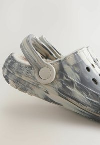 Sabots bleu-gris avec un motif marbré. Fabriqués en plastique, dotés de trous de ventilation, d'un intérieur en peluche et d'une sangle à l'arrière pour un maintien sécurisé.