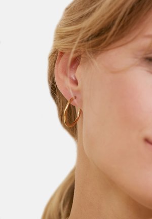 Gold hoop earring with a smooth, shiny finish, circular shape, and a medium size, displayed on a model's ear.