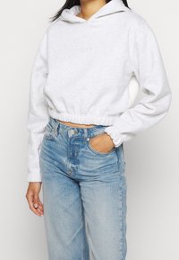 Cropped gray hoodie with long sleeves, elastic waist, and sewn logo detail. Paired with light blue high-waist denim jeans.