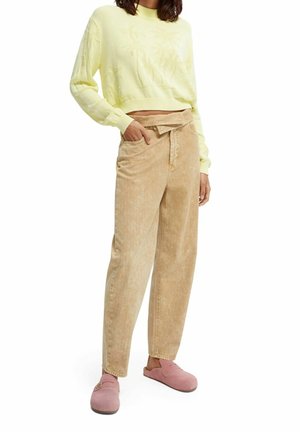 Lichtgele cropped trui, beige corduroy broek en roze instapklompen. De trui heeft een gestructureerde afwerking; de broek heeft een ontspannen pasvorm.