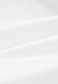 Tissu blanc lisse avec de douces plis créant des lignes diagonales et des ombres douces à la surface.