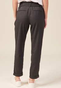 Kolgrå byxor med skräddarsydd passform, två bakfickor, uppvikta benslut och en mjuk textur, i kombination med vita sneakers.