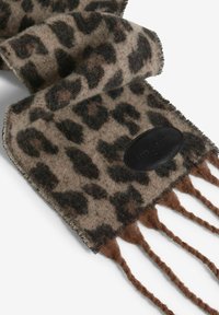 Šál s leopardím vzorom vyrobený z mäkkej látky, so strapcami a čiernou koženou etiketou s embosovanou značkou. Farby zahŕňajú hnedú, pieskovú a čiernu.