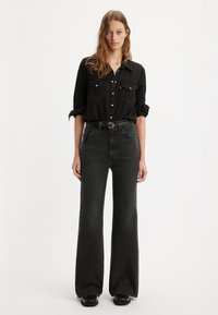 Sorte denimskjorte med knapper foran og to brystlommer, kombinert med høy midje sorte slengbukser og svarte sko.
