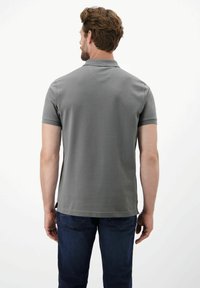 Grijze polo met korte mouwen, gladde textuur en een klassieke kraag, gecombineerd met donkerblauwe jeans. Achteraan zicht met geen zichtbare logo's.