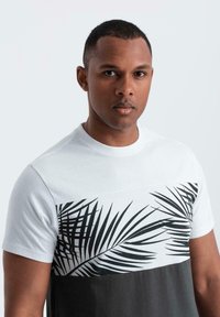 Tričko s krátkým rukávem s bílou horní částí, na které je černý potisk palmových listů, a kontrastní tmavě šedou spodní částí. Materiál je směs bavlny.