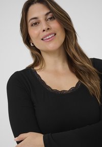 Black long-sleeve top with ribbed texture and a lace-trimmed neckline, worn by a person with brown hair and a neutral background.