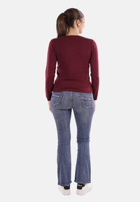 Maglietta a maniche lunghe bordeaux abbinata a jeans a zampa d'elefante di lavaggio medio. L'outfit presenta una silhouette aderente e un design base con dettagli minimi.