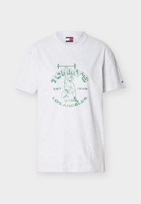 Λευκό κοντομάνικο μπλουζάκι με πράσινο σχέδιο ενός αρσιβαρίστα που κρατά μια μπάρα με βάρη, με την επιγραφή "Tommy's Gym Los Angeles Est 1985" στο μπροστινό μέρος.