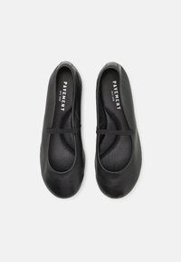 Ballerines en cuir noir avec un bout rond, dotées d'une petite sangle sur le cou-de-pied et d'une semelle intérieure texturée pour une meilleure adhérence.