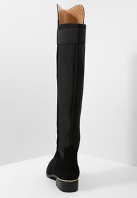 Black knee-high boot with a sleek, smooth exterior, fabric upper, leather lining, a low heel, and gold accent at the base.