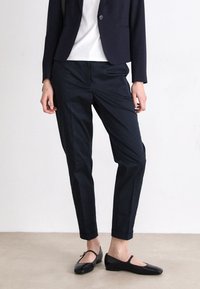 Navy blue tailored trousers made from a smooth fabric, featuring a straight cut and rolled cuffs, paired with black flat shoes.