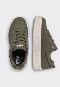 Zelené plátěné tenisky s texturovaným povrchem, bílou gumovou platformovou podrážkou a charakteristickým logem na boku. Mají kulaté tkaničky a průvleky.