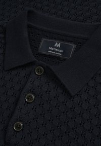 Polo à manches courtes bleu marine en tissu tricoté texturé, avec col, trois boutons foncés et une étiquette portant la marque "Matinique".