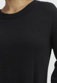 Czarny dzianinowy sweter z okrągłym dekoltem, lekko teksturowany materiał, długie rękawy i luźny krój.